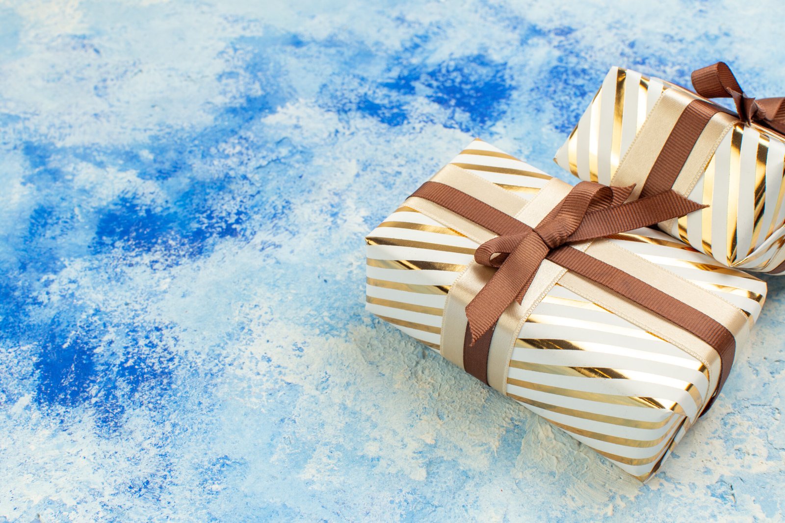 Two gold and white striped gift boxes with brown ribbons on a blue textured background.